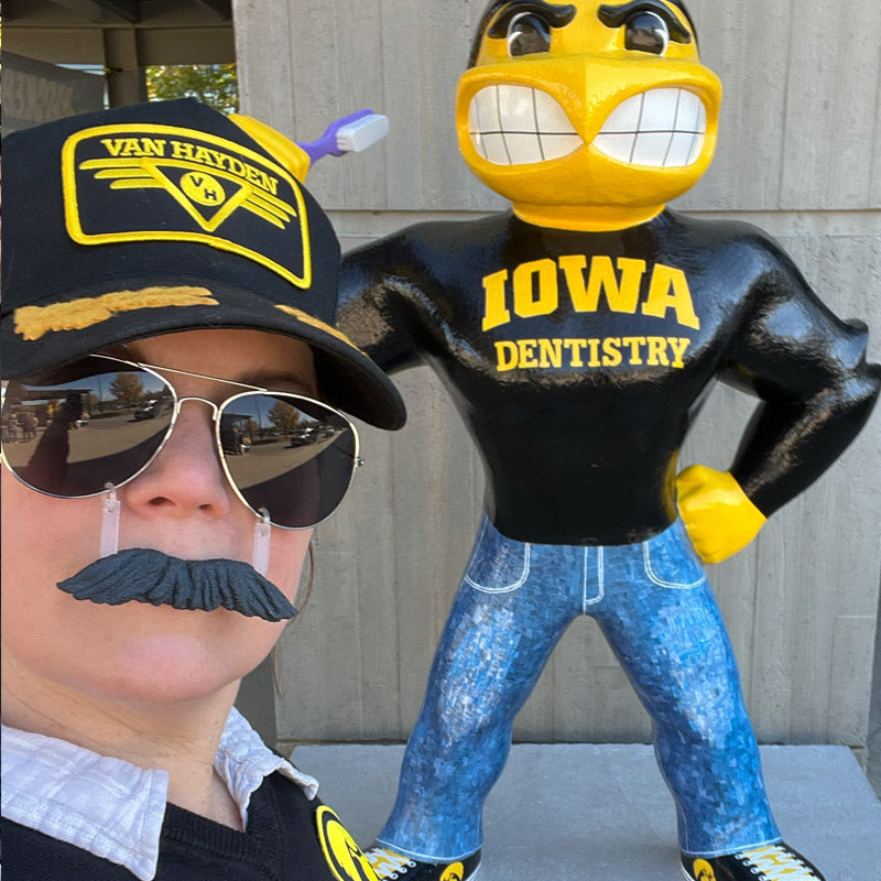 Gidget Van Hayden wearing a trucker hat and sunglasses next to a Herky wearing a 'Iowa Dentistry' shirt