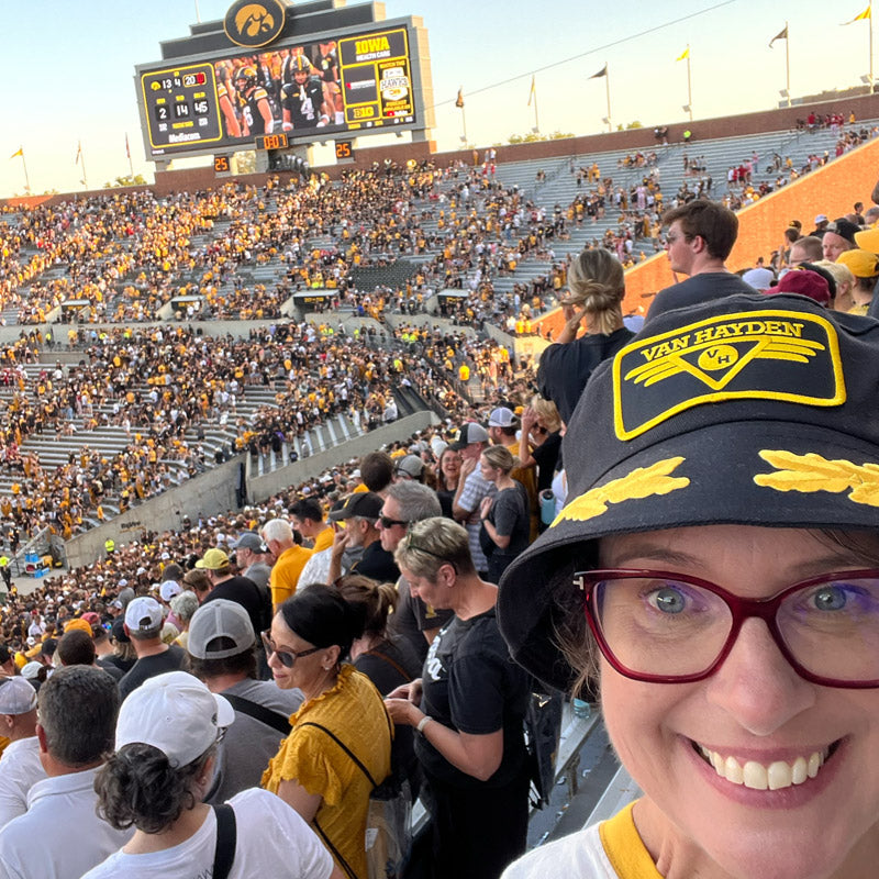 Merch girl Kristy wearing a Van Hayden bucket hat in Kinnick stadium filled with Iowa spectators
